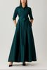 A model wearing a dark teal green maxi dress with three-quarter sleeves, a button-down collar, and a matching self-tie belt at the waist. The brand names 'terri jon' and 'terrie freeman' are printed in the top left corner against a light gray studio background.
