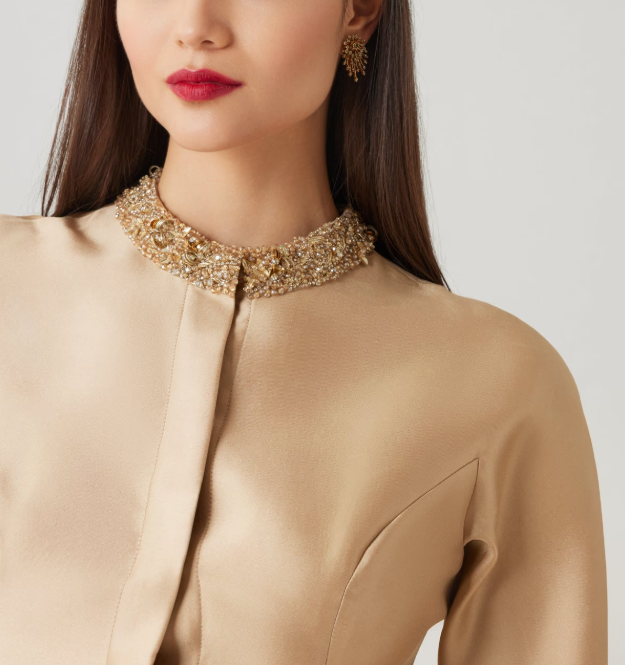 Woman wearing a beige dress with a decorative collar against a plain background